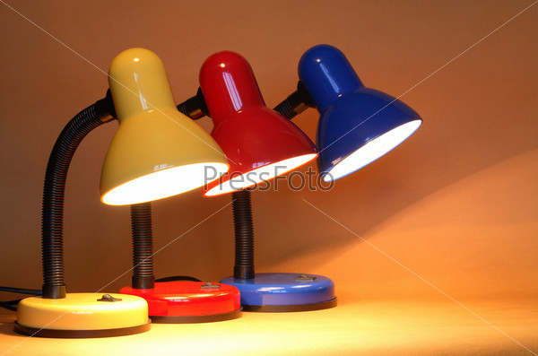 Three colored modern luminous desk lamps on yellow background with beam of light