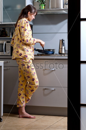 Beautiful young woman is cooking breakfast. She is dressed in sleepwear.