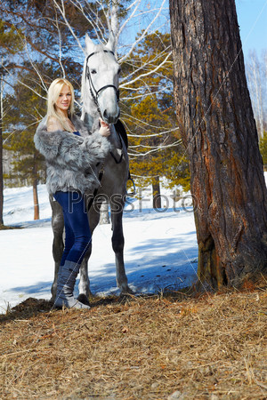 outdoor portrait of beautiful blonde girl in furs with pale horse in sunny winter forest