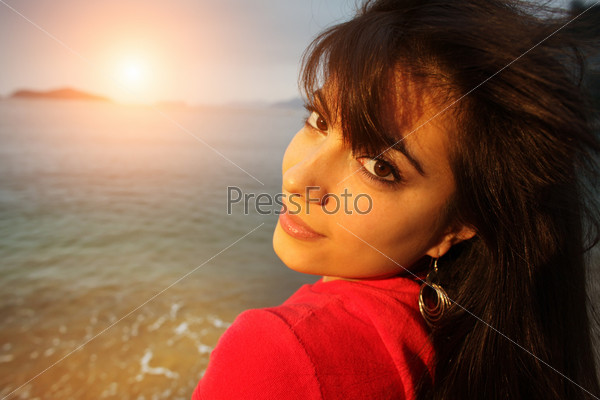 Young beautiful woman at beach at sunset looking back at camera.