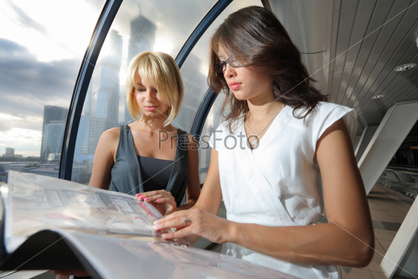 Two businesswomen looking into papers in futuristic interior