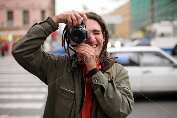 Молодой человек с фотоаппаратом на фоне  городской улицы