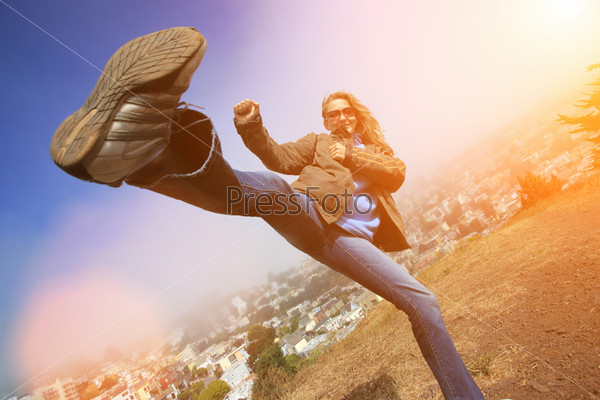Young woman fooling around doing high kick ontop of the Kite Hill, San Francisco, California, USA.