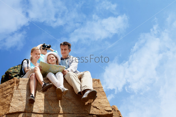 Portrait of family of travelers sitting on rocky cliff and looking at map