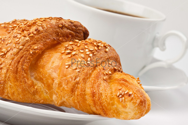 A cup of coffee and a croissant with sesame seeds
