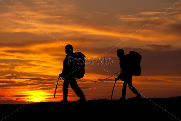 silhouette of two walking rock climbers on sunset sky