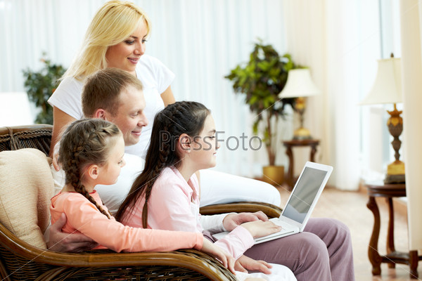 Image of friendly family sitting on the sofa and looking at laptop