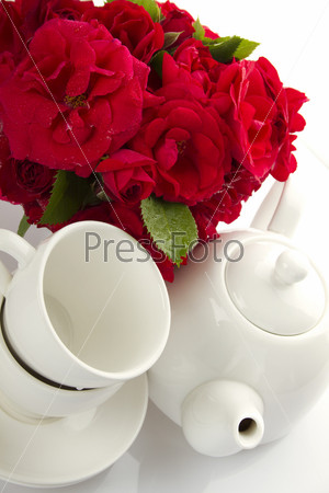 White crockery for tea kettle, two cups and saucers and a bouquet of red roses in a small iron bucket