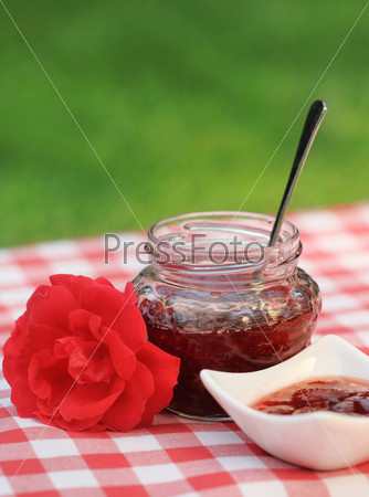 Jar of rose jam and one rose on the napkin