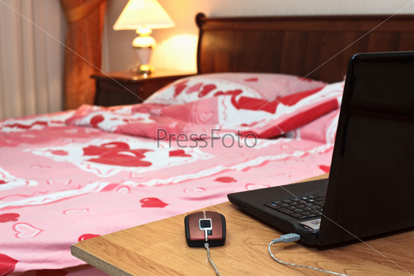 Laptop on table near bed in bedroom at evening time