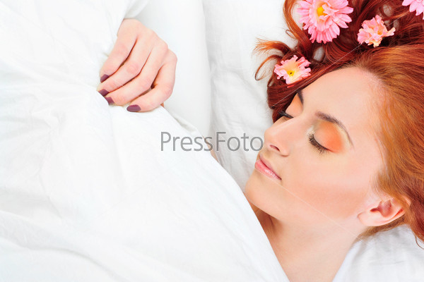 Closeup portrait of young beautiful caucasian woman with red hair lies on bed with fresh pure white linen. Flowers in her head.
