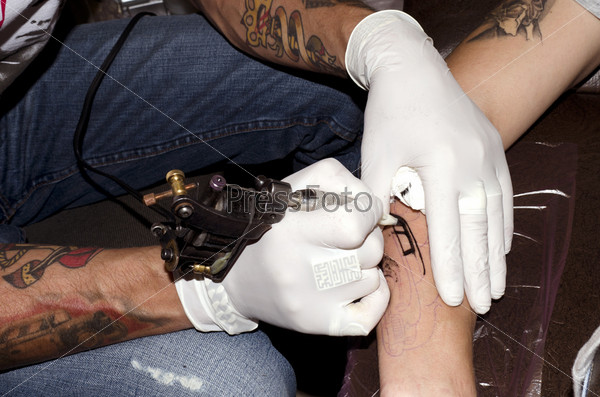 Мастер делает татуировку на руке