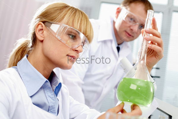 Serious clinician looking at flask with liquid in laboratory
