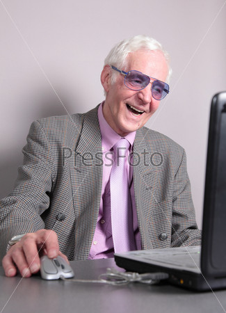 Old man looks in the screen of notebook laughs. isolated against grey background