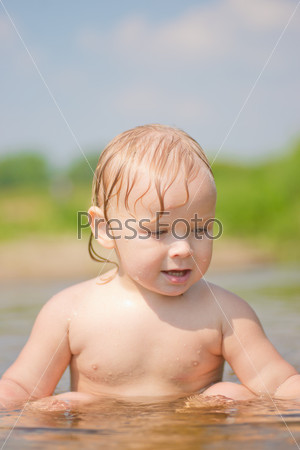 Adorable baby sit in river and play with sand and wood branch