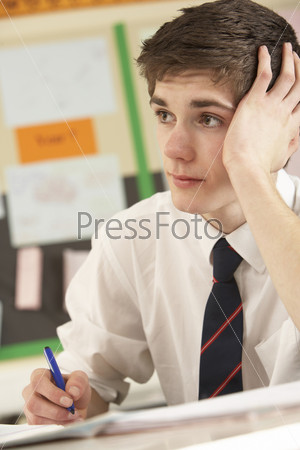 Stressed Male Teenage Student Studying In Classroom