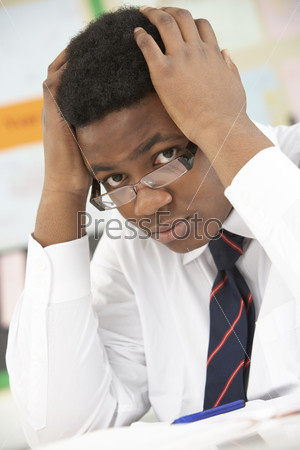 Stressed Male Teenage Student Studying In Classroom, stock photo