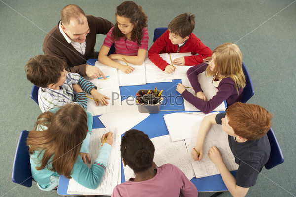Schoolchildren Working Together At Desk With Teacher