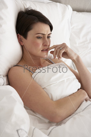Обеспокоенная женщина лежит в постели без сна
