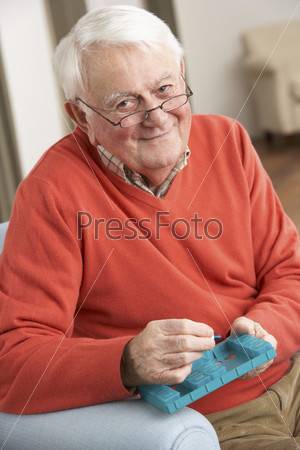Senior Man Sorting Medication Using Organiser At Home