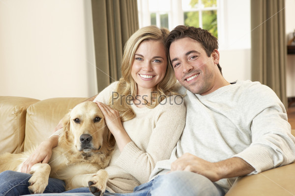 Молодая счастливая пара с собакой, сидя на диване
