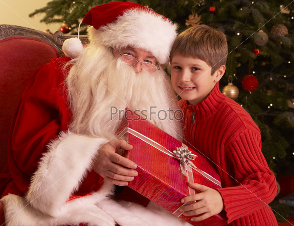 Santa Claus Giving Gift To Boy In Front Of Christmas Tree
