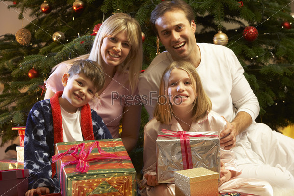 Family Opening Christmas Present In Front Of Tree