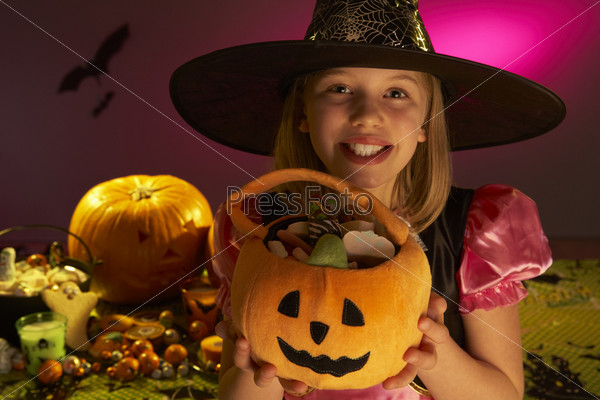 Девочка в костюме ведьмы на празднике Хэллоуин с резной тыквой в руках