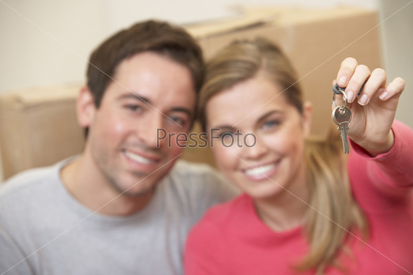 Молодая пара на фоне картонных коробок в новой квартире, девушка с ключами в руке