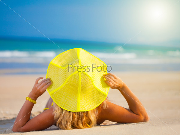 Woman in yellow hat sunbathing on the beach