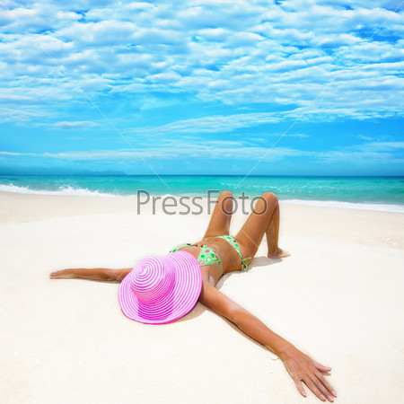 Девушка в розовой шляпе загорает на пляже