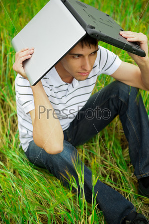 A smiling man with laptop outdoor lies relaxed on the ground in grass