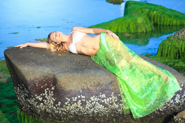 Beautiful woman like mermaid laying on the rock