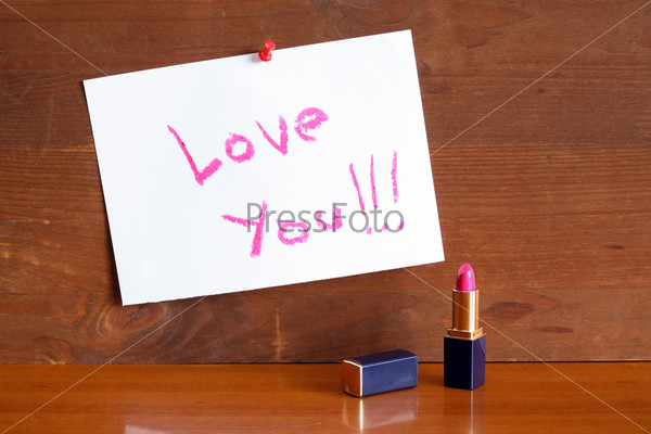 Inscription Love You on white paper made with pink lipstick on wooden background