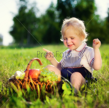 Little boy with a basket of fruit sits on a grass, stock photo