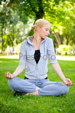 Portrait of young woman meditating in pose of lotus on green grass on meadow at summer park under tree