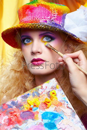 Девушка-художник делает макияж при помощи кисти и палитры