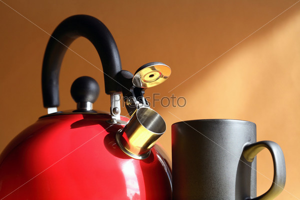 Closeup of red metal kettle near black mug on background with sunbeam, stock photo