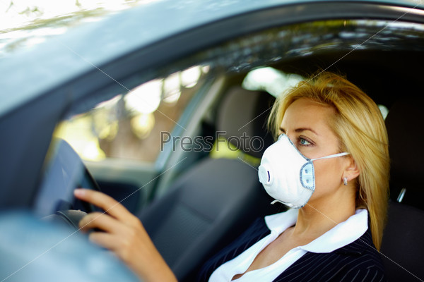 Photo of blond female wearing respirator while driving car in polluted area, stock photo