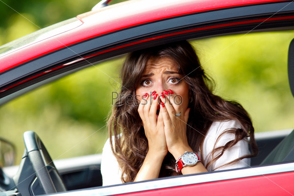 Молодая девушка испуганно смотрит из окна красного автомобиля