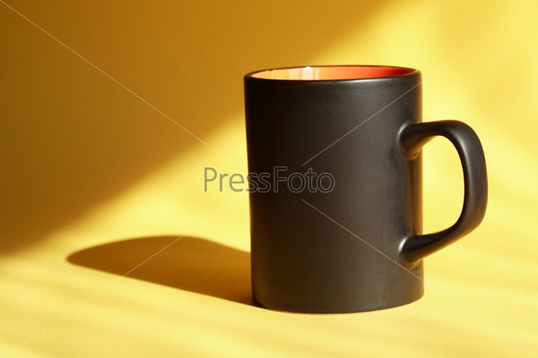 Black mug standing on nice yellow background with sunbeam, stock photo