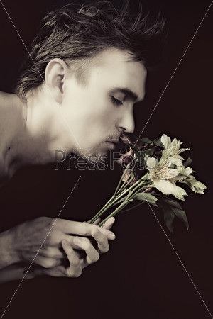 face of the young men sniffing bouquet of flowers on a black background