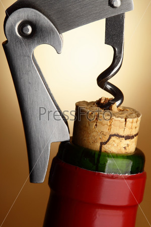Opening wine bottle by corckscrew over yellow background