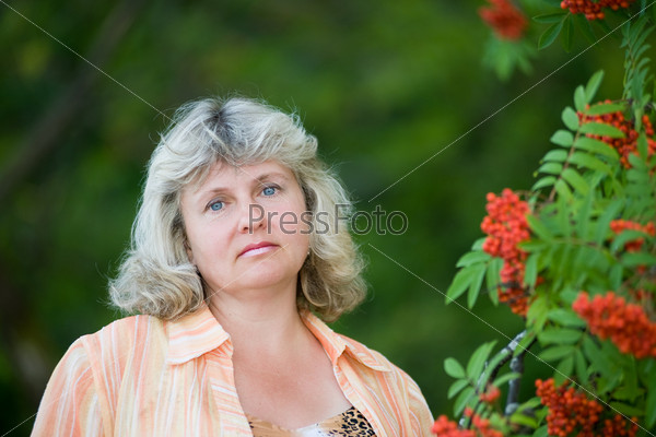The beautiful woman in forty five years near to mountain ash bushes.