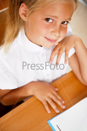 Image of smart child reading interesting book in classroom. Vertical Shot. Looking at camera