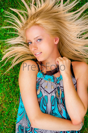 Young woman laying on green grass with hair like a sun around her head. Photo from above