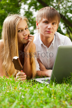 College students using laptop on campus lawn and eating ice cream