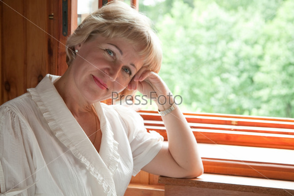The mature woman at the open window with a kind on wood