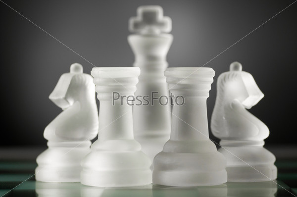 glass chess pieces are defending the king on board in dark