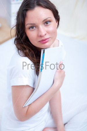 Young woman with a notebook studying at home sitting relaxed on bed